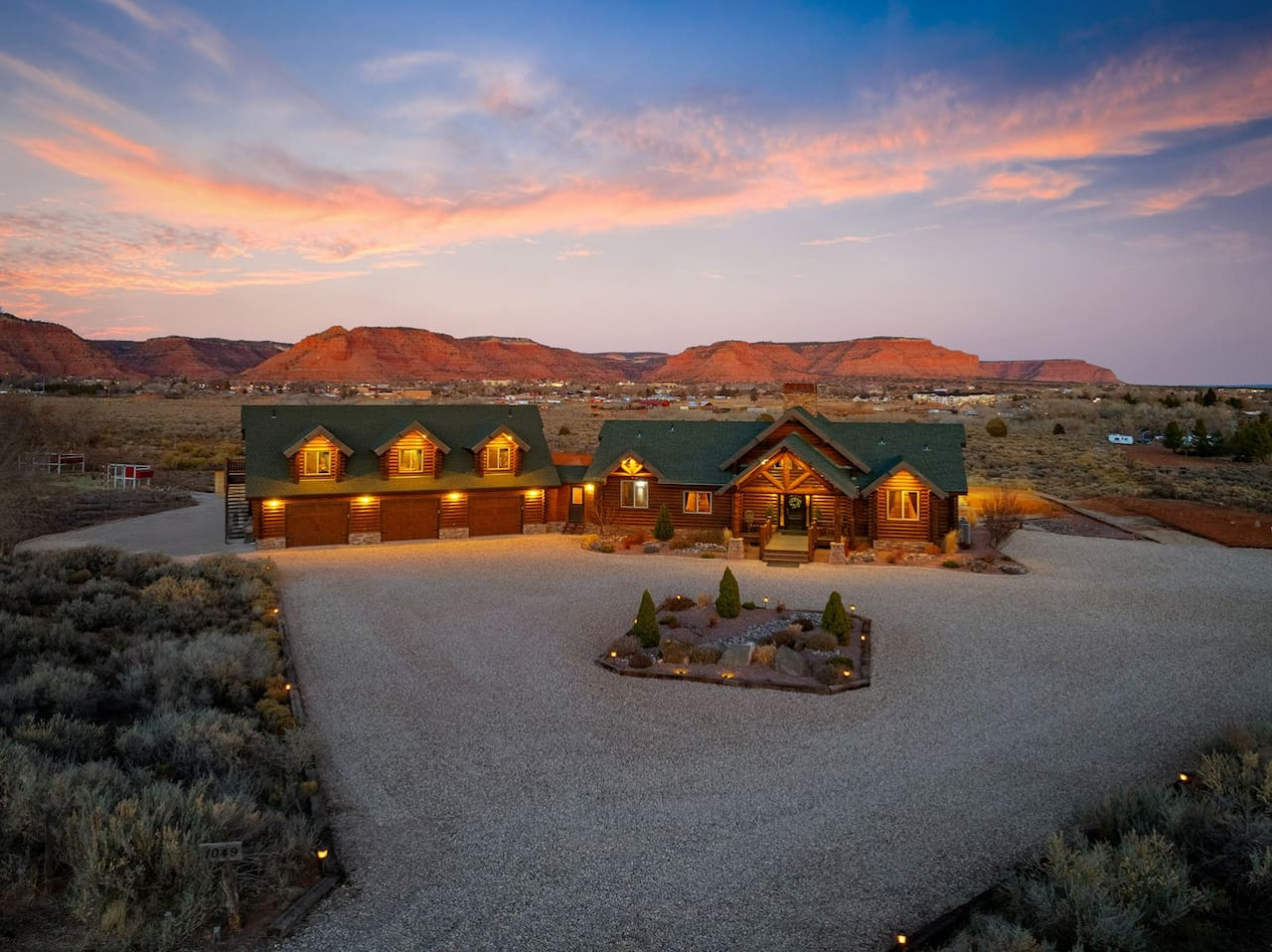 The Blackhawk Cabin, a Prime Properties home in Kanab, Utah, lit up at dusk with red cliffs behind it